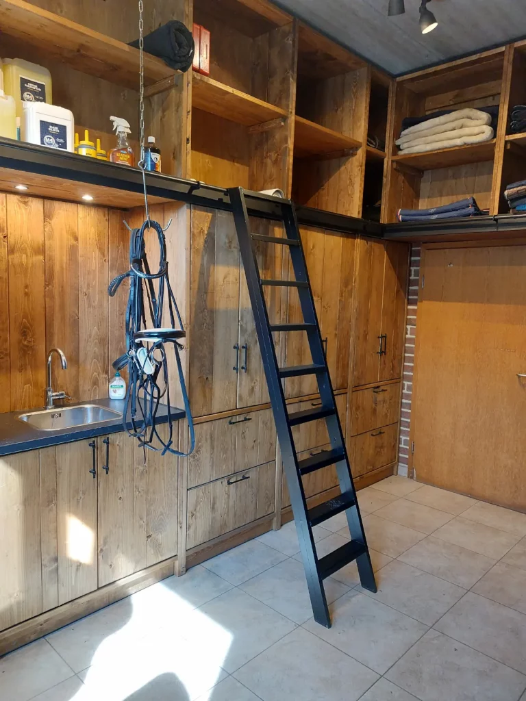 Hoge zadelkamer kasten eikenhout zwarte accenten. Gesloten en open kasten, poetshaak met hoofdstellen, wasbak, verschuifbare ladder, kasten boven deur.
